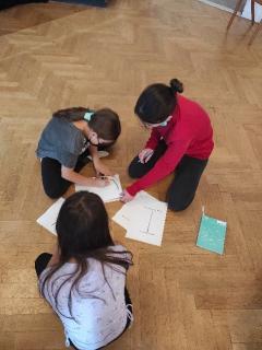 Drei Mädchen* sitzen auf dem Boden und schreiben Buchstaben auf Plakate.